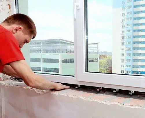 Logu meistars veic PVC loga montāžu daudzdzīvokļu ēkā.